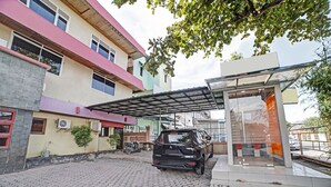 A black SUV parked in a covered parking area with a modern building featuring a glass facade and a red roof.