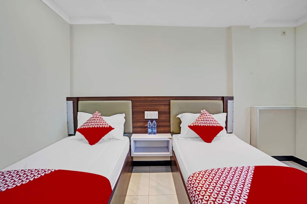 A hotel room with two single beds, a nightstand with a lamp, and a small table with two bottles.