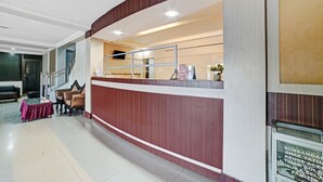 A reception area with a wooden reception desk, a seating area with a table and chairs, and a staircase in the background.