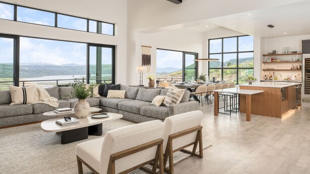 Ein geräumiges Wohnzimmer mit einem großen, grauen Ecksofa, einem Couchtisch und einer Küchenzeile mit Bar und Kochinsel.