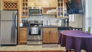 A kitchen with wooden cabinets, stainless steel appliances, and a dining area with a purple tablecloth. - Romance in the City - 1 Bdrm Studio in Downtown! (St. Petersburg)