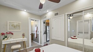 A hotel room with a bed, a desk with a chair, a vanity, and a bathroom visible through an open door. - Romance in the City - 1 Bdrm Studio in Downtown! (St. Petersburg)