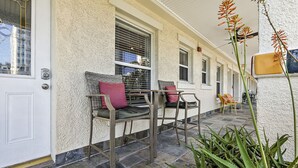 A covered outdoor seating area with a white door, a window with blinds, and a potted plant. - Romance in the City - 1 Bdrm Studio in Downtown! (St. Petersburg)