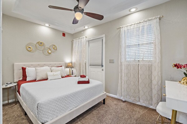 A neatly arranged bedroom with a bed, bedside tables, a desk, and a ceiling fan.