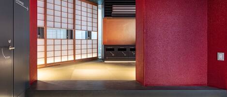 A hotel lobby with a traditional Japanese-style room, a red textured wall, and a modern reception desk.