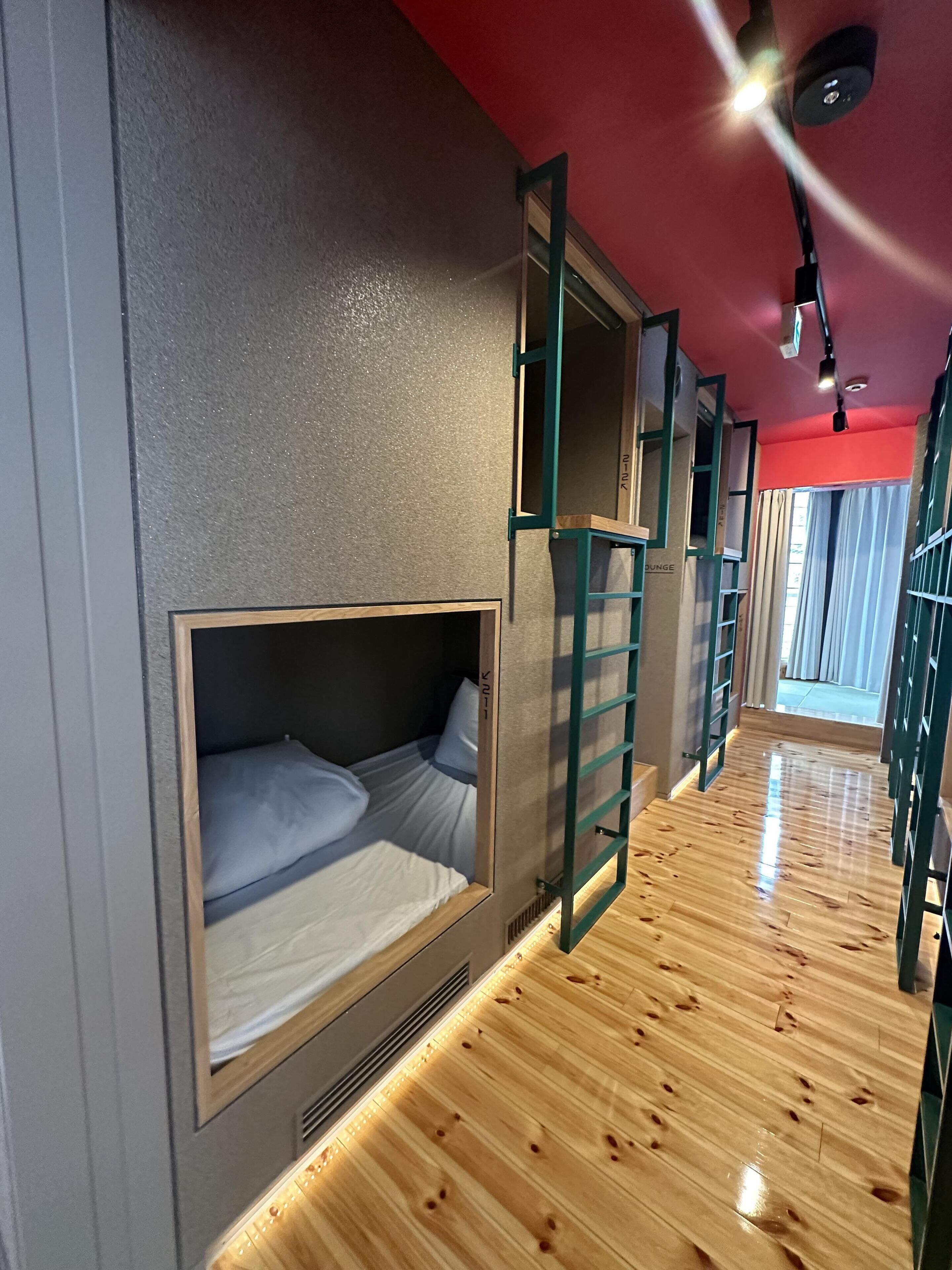 A room with bunk beds, a wooden floor, a red ceiling, and a window with curtains.