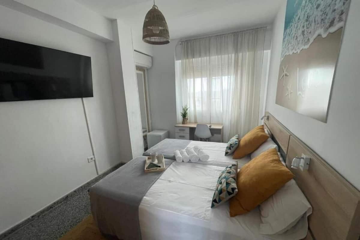Een moderne slaapkamer met een bed, nachtkastjes, een televisie en een raam met gordijnen.