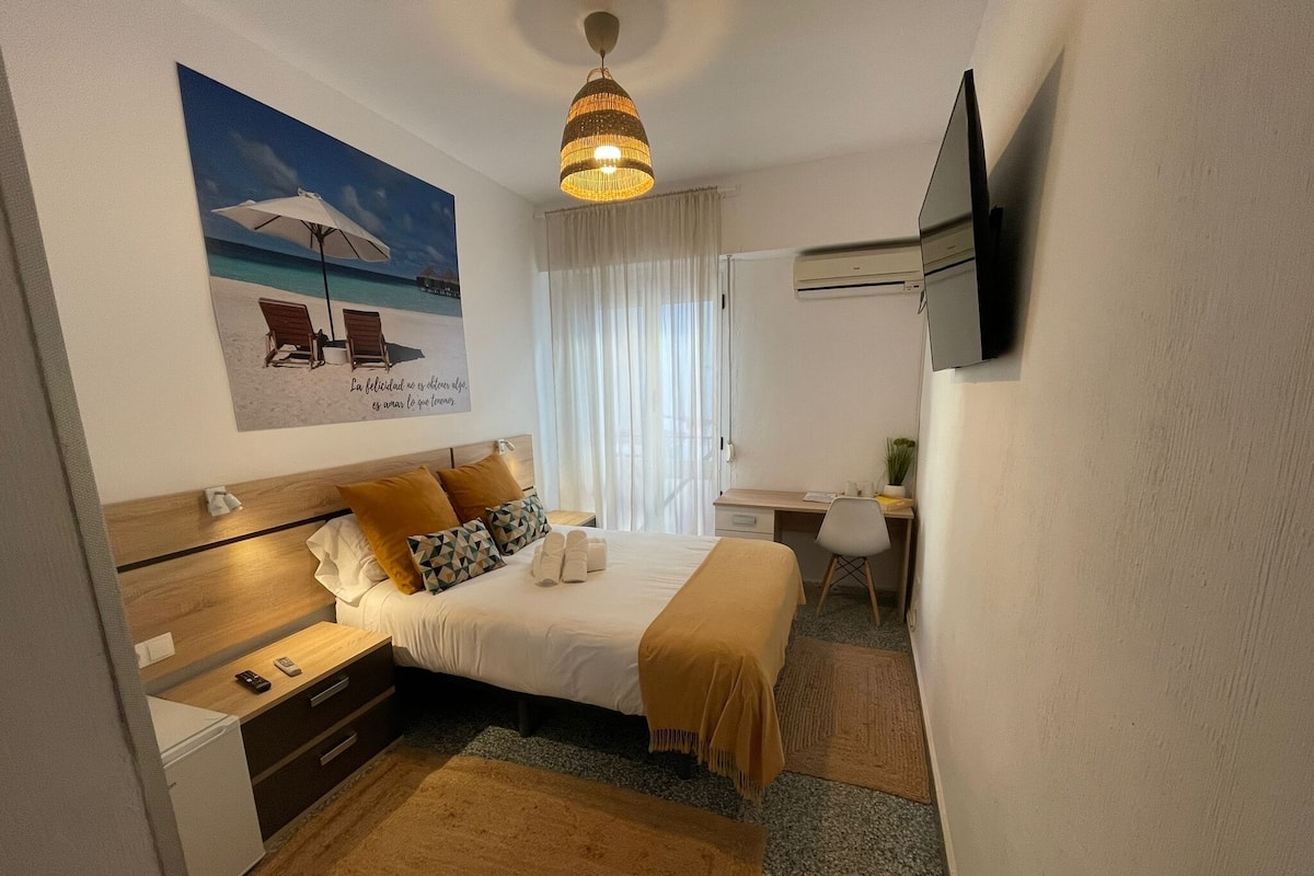 Een hotelkamer met een bed, een bureau, een stoel, een televisie en een schilderij van een strand.