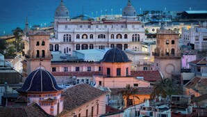 A historic building with multiple domes and a prominent clock tower, surrounded by other buildings and palm trees. - Hostal Ventura Premium  (Alicante)