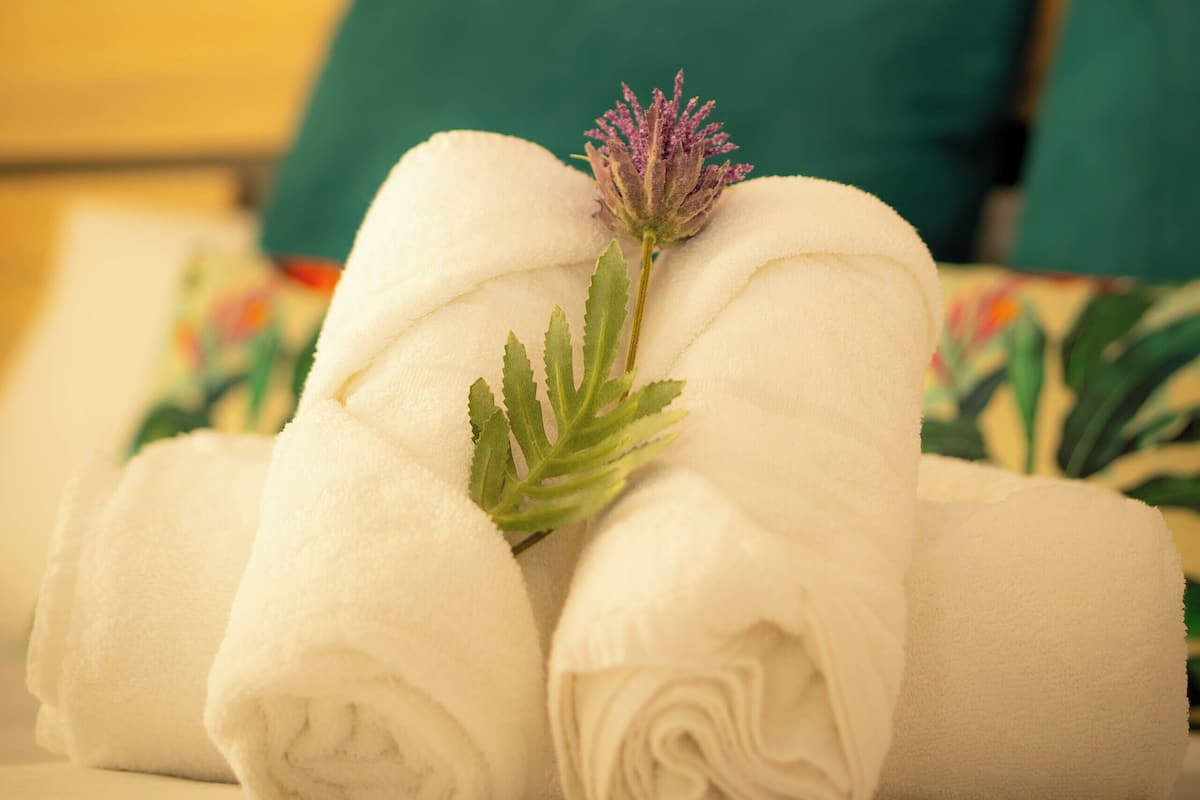 Een net opgemaakt bed met opgerolde witte handdoeken en een decoratieve bloem.