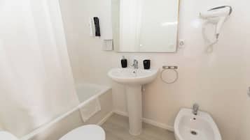 A modern bathroom with a bathtub, a pedestal sink, a bidet, and a hairdryer mounted on the wall.