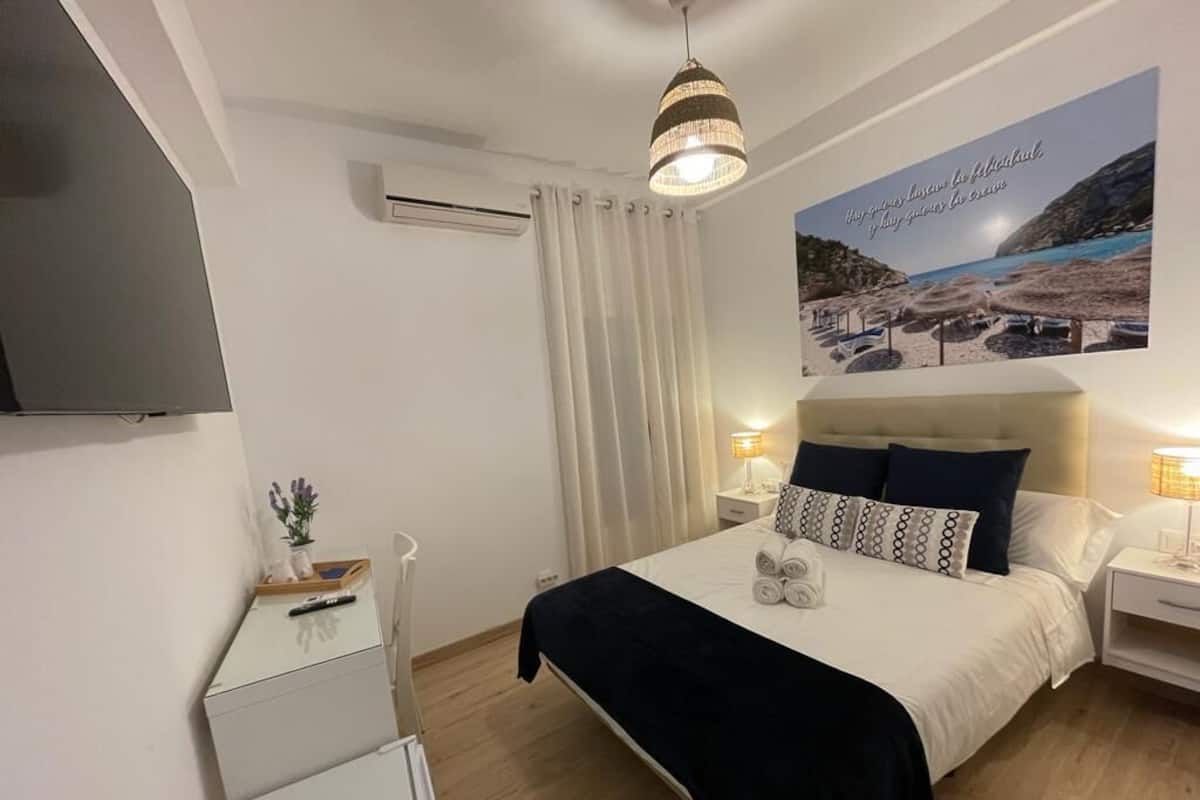 Een slaapkamer met een bed, nachtkastjes, een televisie, een poster en een plafondlamp.