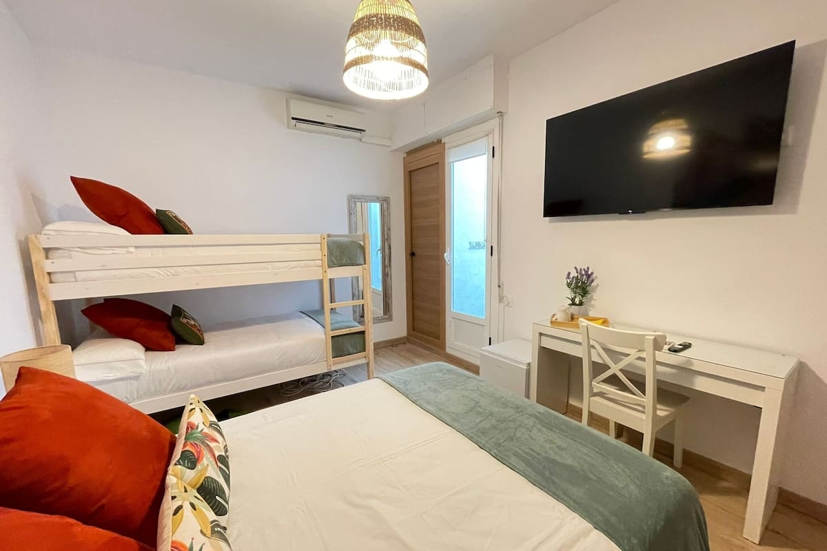 Een slaapkamer met een stapelbed, een bureau, een stoel, een televisie en een raam.