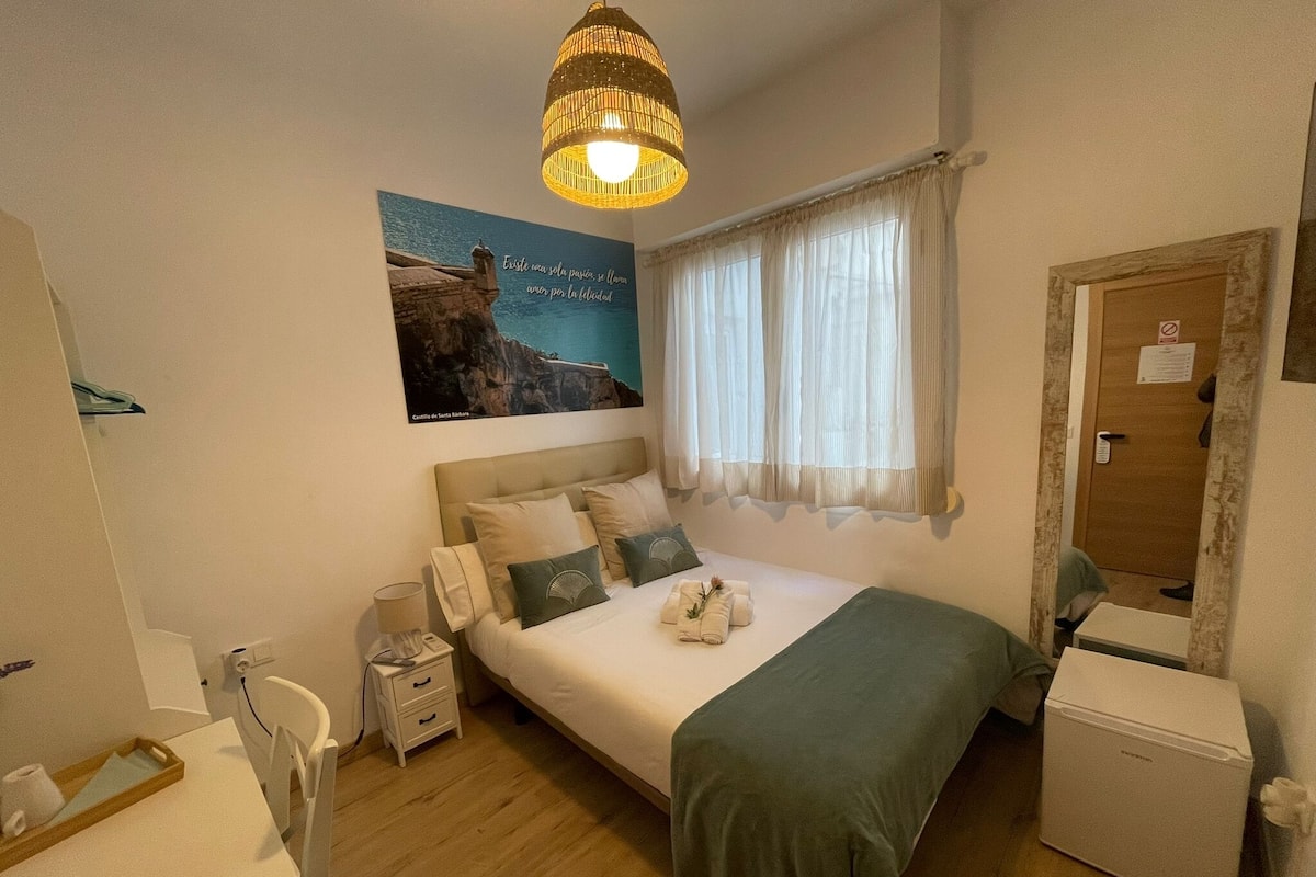 Een slaapkamer met een bed, nachtkastjes, een dressoir, een spiegel, een raam met gordijnen, een wandlamp en een poster.