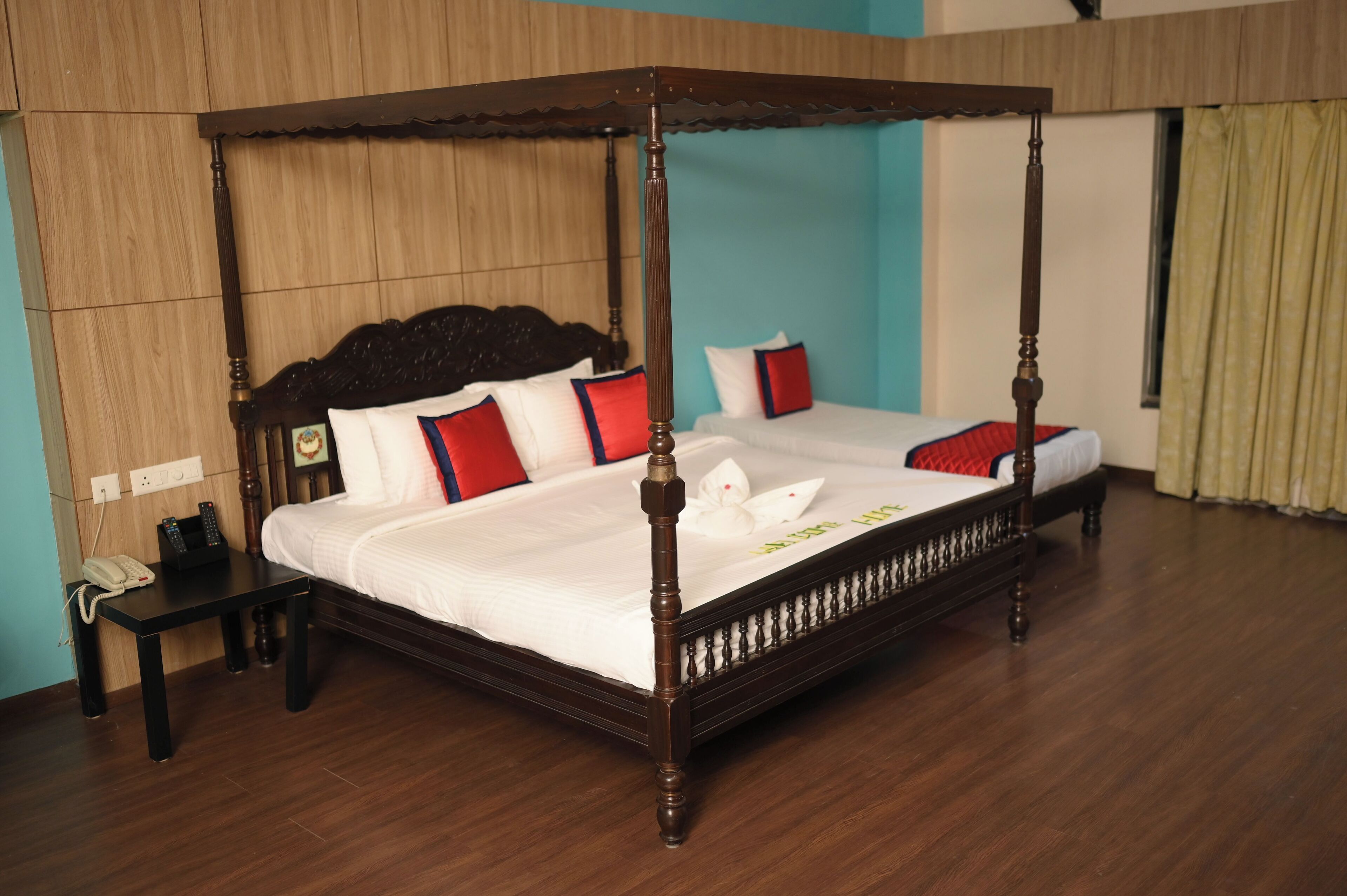 A four-poster bed with white bedding and red pillows, a bedside table with a phone, and a wooden floor.