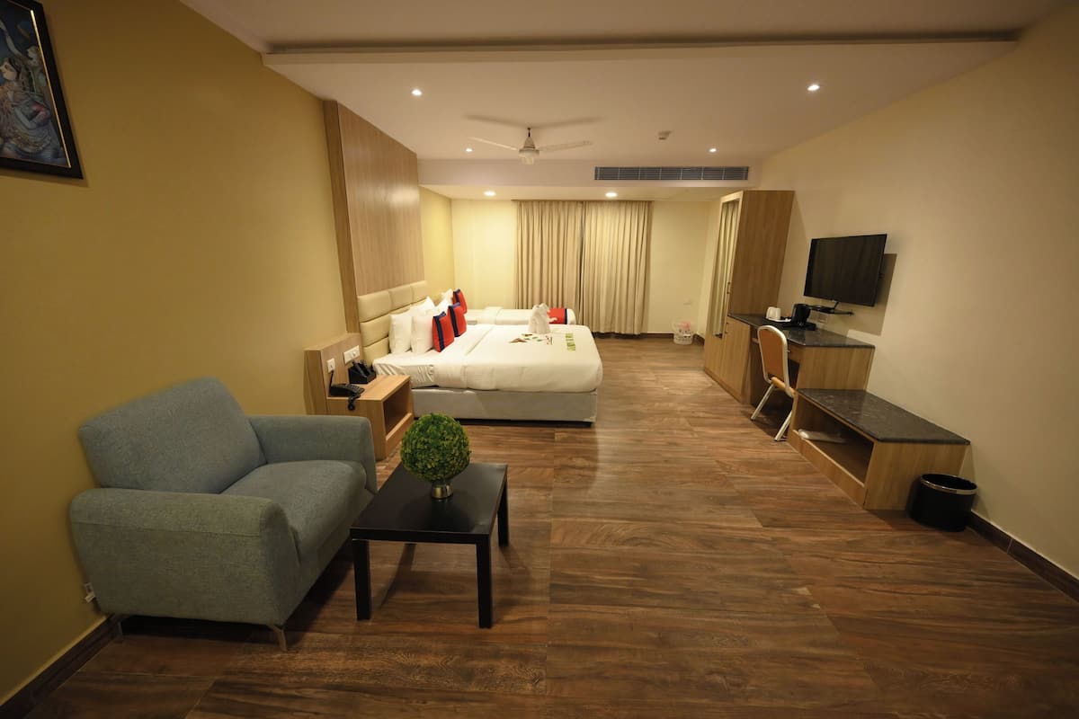 Quarto de hotel com cama, sofá, escrivaninha, televisão e ventoinha no teto.