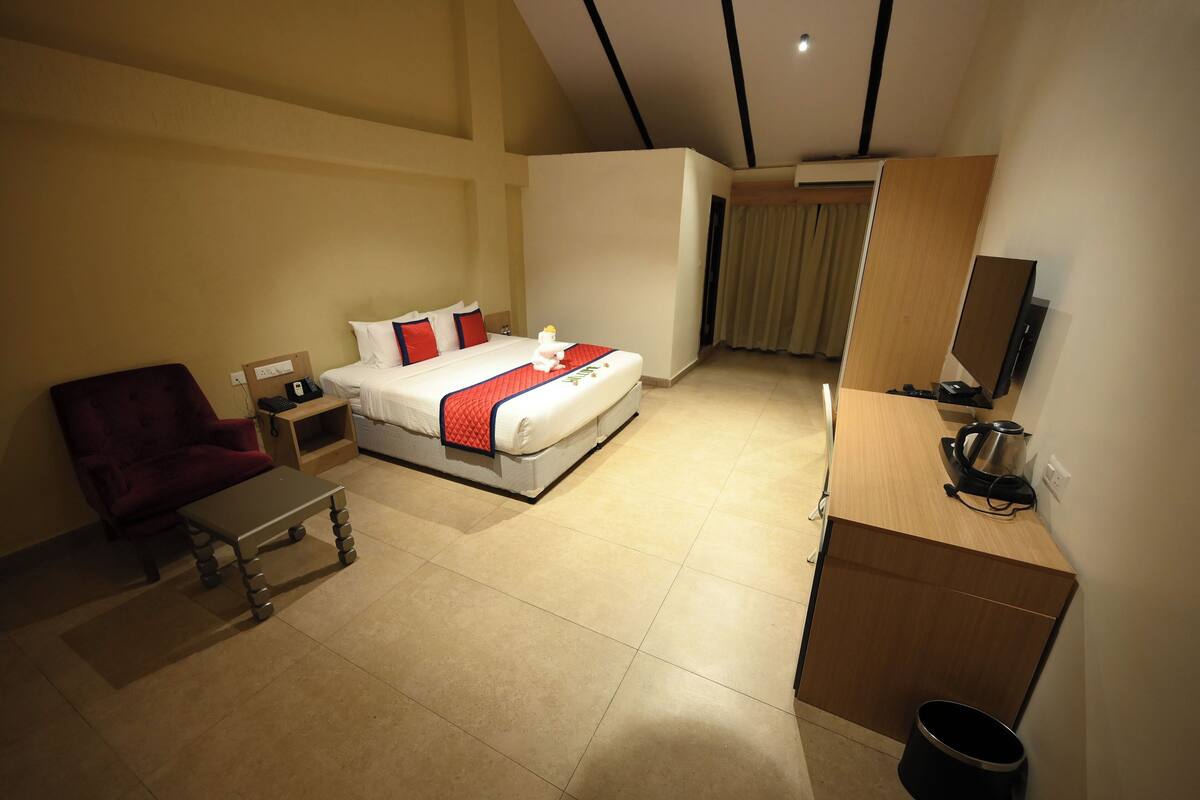 Quarto de hotel com cama, escrivaninha, cadeira, televisão e uma pequena cozinha.