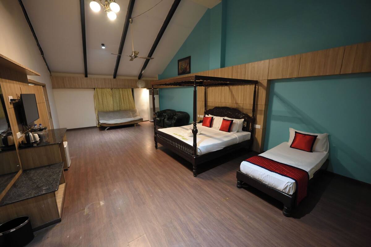 Quarto de hotel com uma cama grande, uma cama menor, uma mesa e uma televisão.
