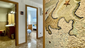 A hallway with a bathroom on the left, a bedroom with a bunk bed in the center, and a mosaic wall with a starfish design on the right. - ROCAMAURA I D 1-2 (Estartit)