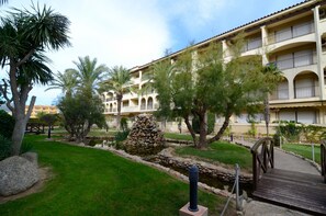 A hotel with a courtyard featuring palm trees, a stone structure, and a wooden bridge. - JARDINS DEL MAR 006 (Estartit)