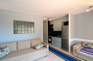 Un salon avec un canapé et une table basse, une cuisine équipée de meubles et d’appareils électroménagers, et un tapis bleu sur le sol.
