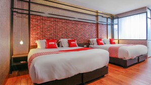 Habitación de hotel con dos camas, una pared de ladrillo y ventanas grandes.