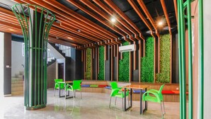 Un espacio interior moderno con techo de madera, sillas verdes, una mesa y una pared verde con vegetación vertical.