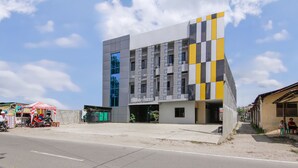 Un edificio moderno con fachada singular, cielo despejado y calle con una motocicleta y una pequeña tienda.