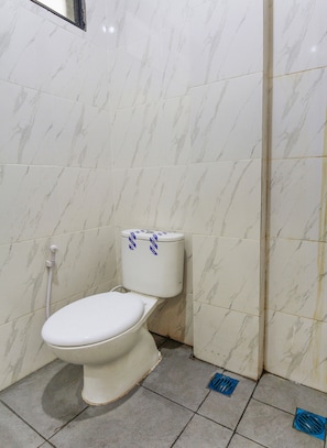 A bathroom with a toilet, marble tiles, and a shower area.