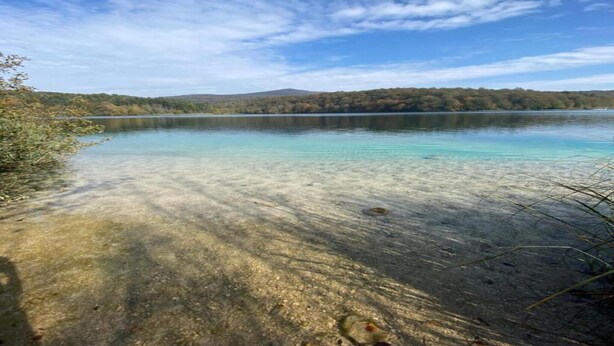 Un llac tranquil amb una riba boscosa i turons allunyats.