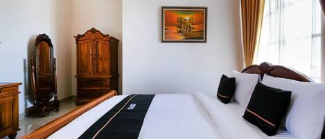 Habitación de hotel con una cama grande, un armario de madera, un cuadro en la pared y una ventana con cortinas.