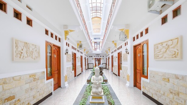 Un largo pasillo con una estatua central, paredes blancas y puertas a ambos lados.