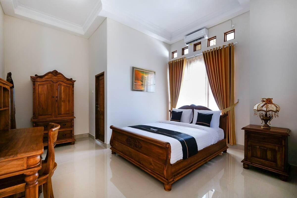 A bedroom with a wooden bed, a wooden dresser, a wooden nightstand, and a painting on the wall.
