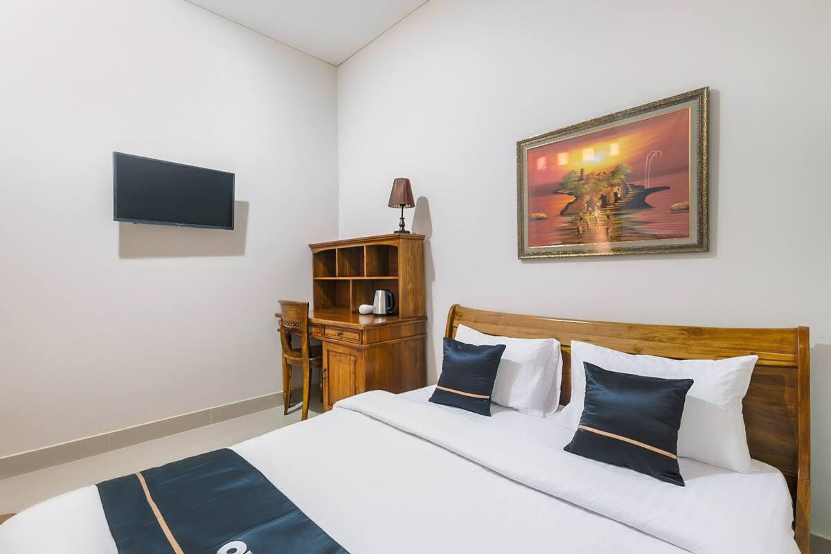 A neatly arranged hotel room with a bed, a wooden nightstand, a TV mounted on the wall, and a painting above the bed.