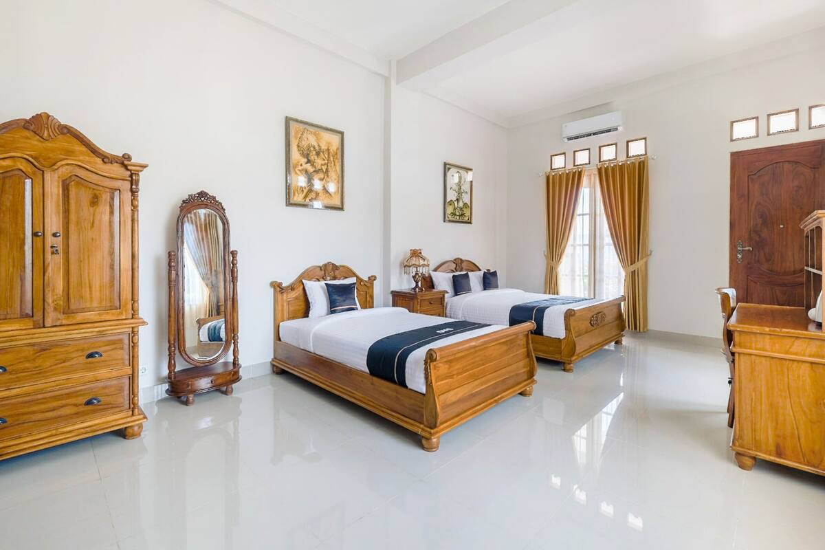 A spacious bedroom with two wooden beds, a large wardrobe, a mirror, and a chandelier.