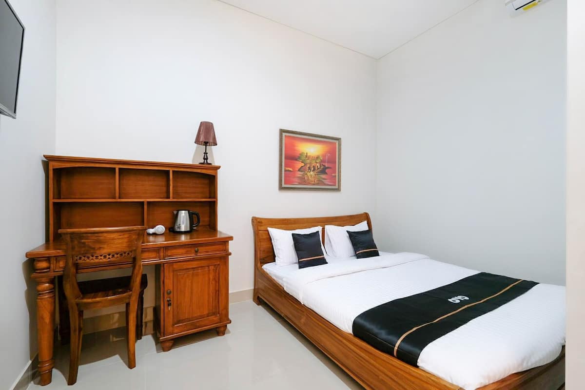 A bedroom with a wooden bed, a desk with a lamp, and a painting on the wall.