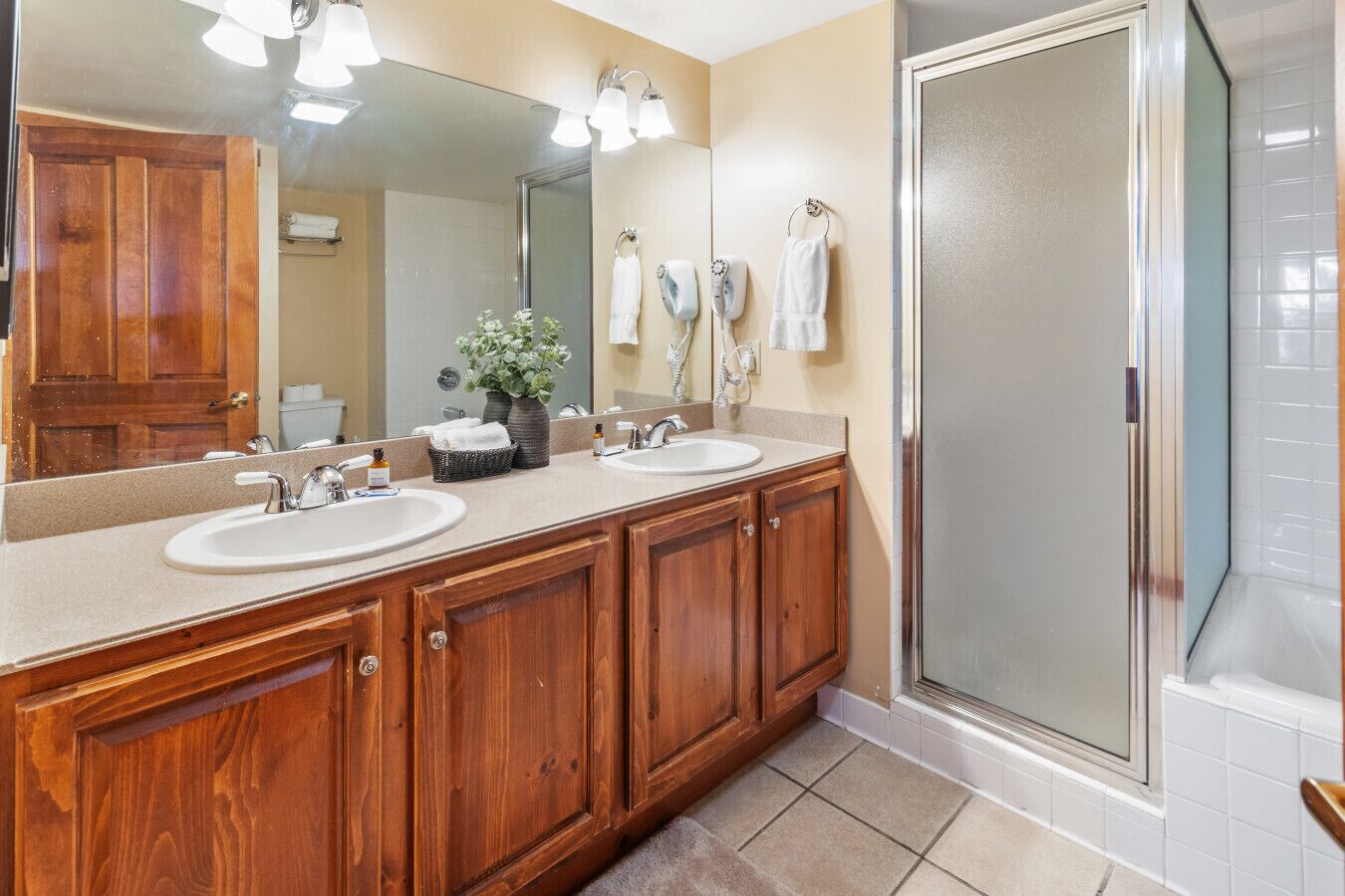 Une salle de bain avec deux lavabos, des meubles en bois, un grand miroir, une douche et un porte-serviettes.