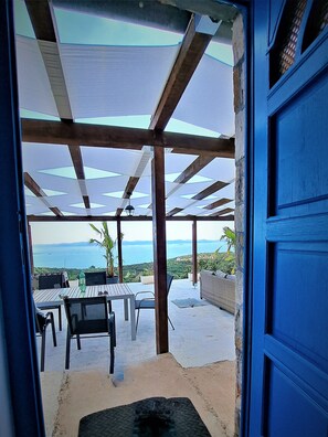 An open doorway leading to a covered outdoor area with a table and chairs, a view of the sea, and a blue door. - Romantic isolated villa with pool surrounded by pure nature. (Tkon)