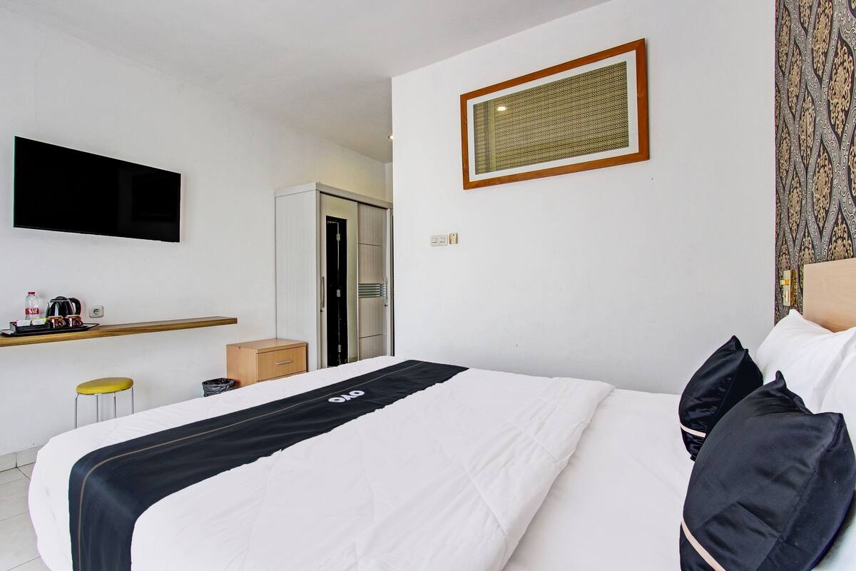 Habitación de hotel con cama, televisor montado en la pared, escritorio pequeño con silla y puerta que da a un baño.