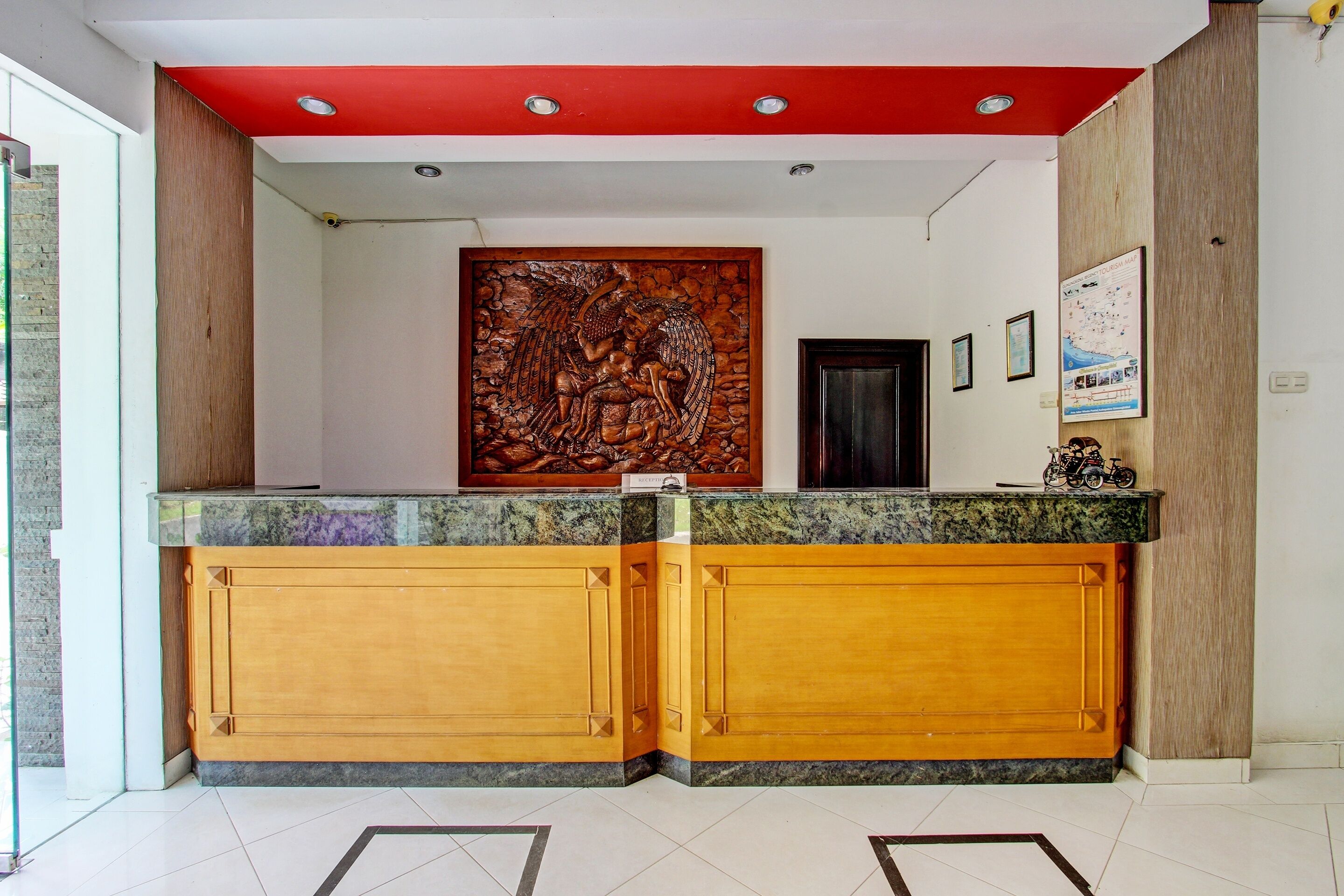 Un espace d’accueil avec un comptoir de réception en bois, une grande sculpture murale et des tableaux encadrés accrochés au mur.