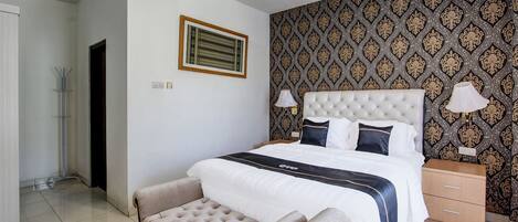 A neatly arranged bedroom with a large bed, a bedside table, a bench, and patterned wallpaper.