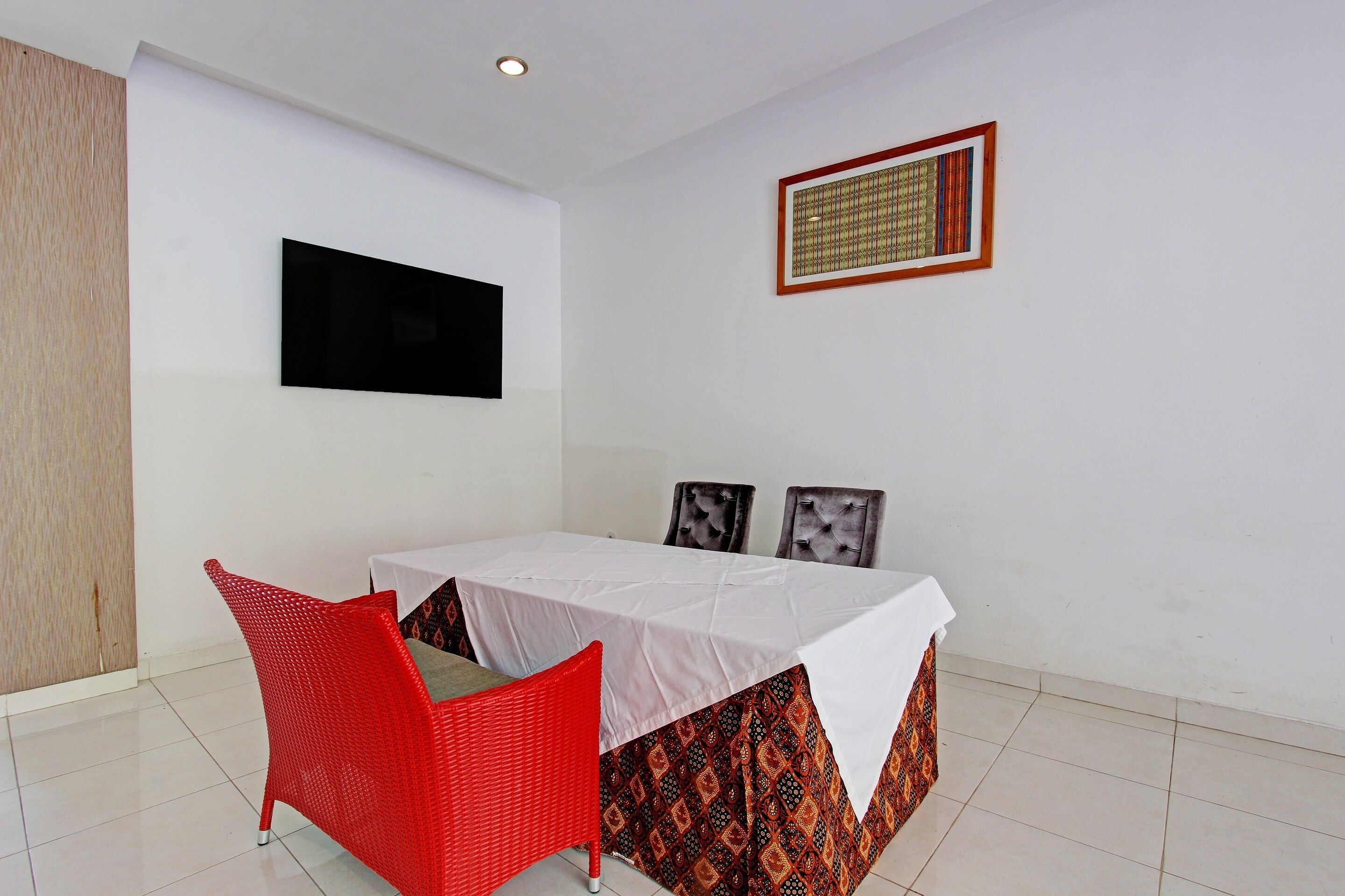 A room with a bed, a red chair, a TV on the wall, and a patterned curtain.