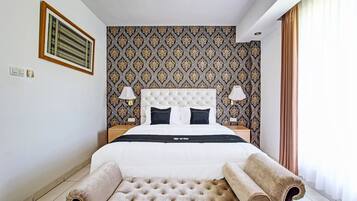 A hotel room with a large bed, two bedside lamps, a tufted headboard, a patterned wallpaper, and a large window with curtains.
