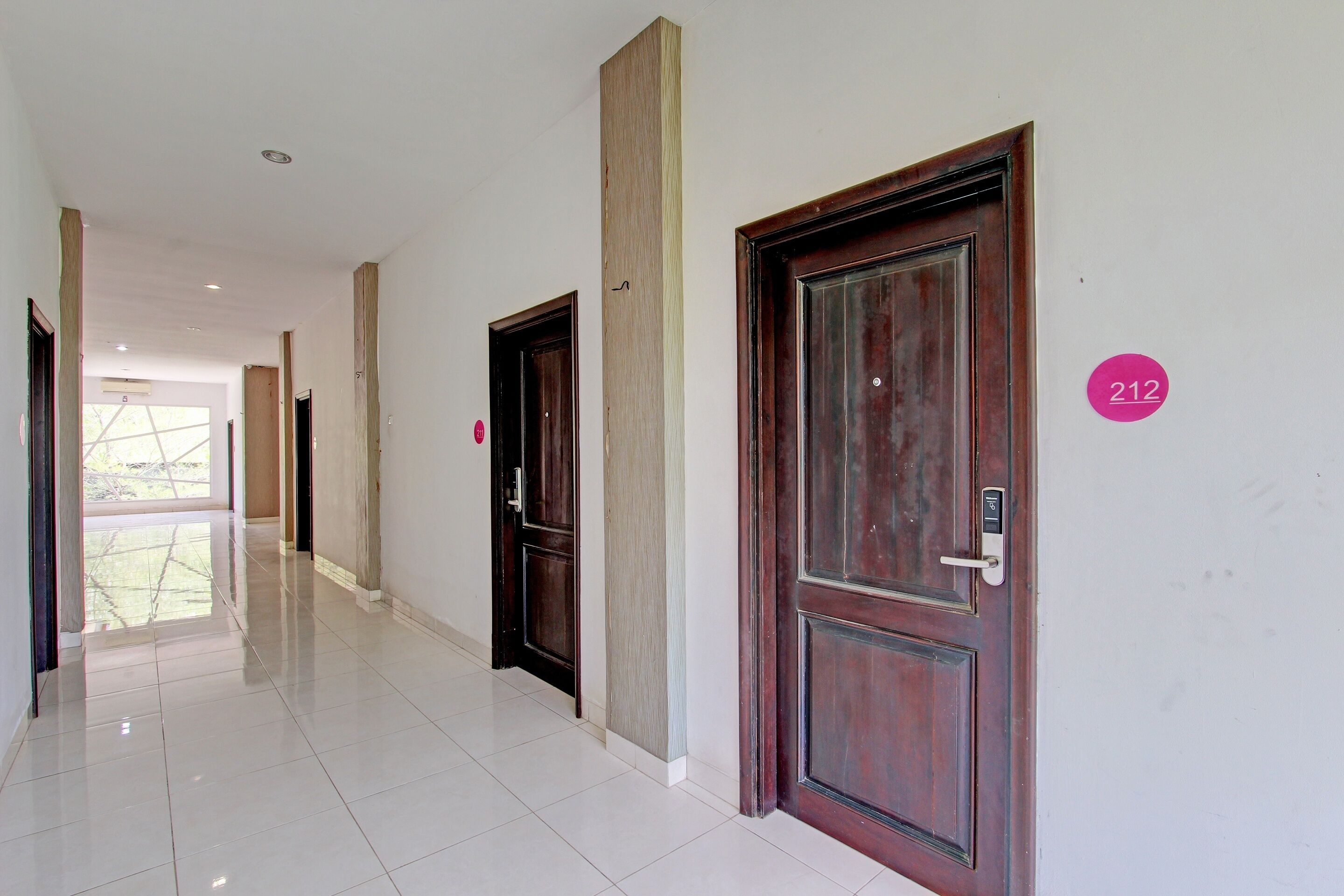 A hallway with two wooden doors, one marked with the number 212, and a bright, tiled floor.