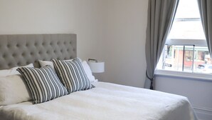 Una cama bien hecha con almohadas a rayas, un cabecero capitonado y una lámpara de noche.