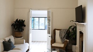 Una sala de estar con un sofá blanco, una silla de mimbre, una chimenea y un televisor sobre una estantería.