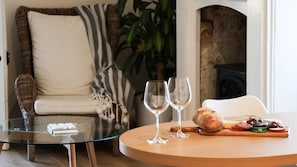 Una sala de estar acogedora con una mesa de centro de vidrio, un sofá de mimbre y una mesa redonda de madera con comida y copas de vino.