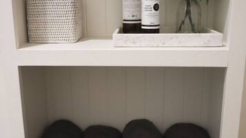 A shelf with a woven basket, two bottles of foot repair cream, and a glass container with a plant.