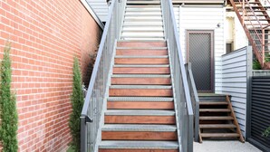 Una escalera estrecha con barandillas metálicas que conduce a una puerta de madera.
