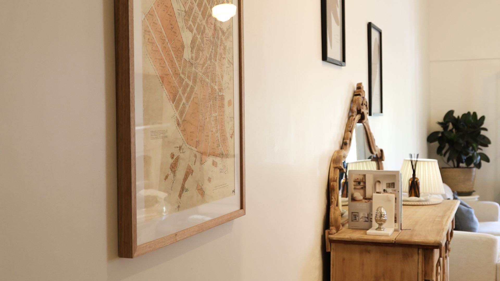 Een lijst met een kaart aan de muur, een houten bijzettafeltje met een lamp en een kamerplant.